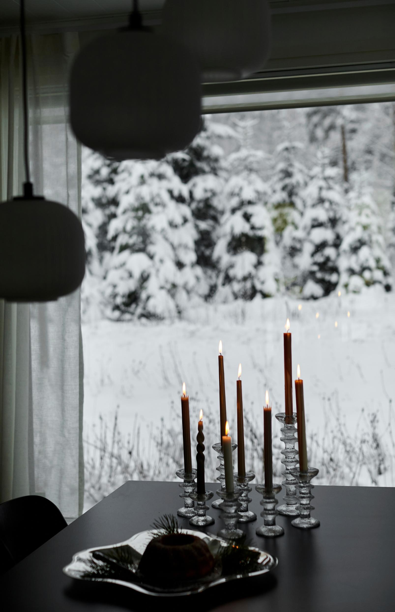 Ultima Thule -kynttilänjalkoja, metallivati, musta pöytä, kynttilöitä ja luminen maisema