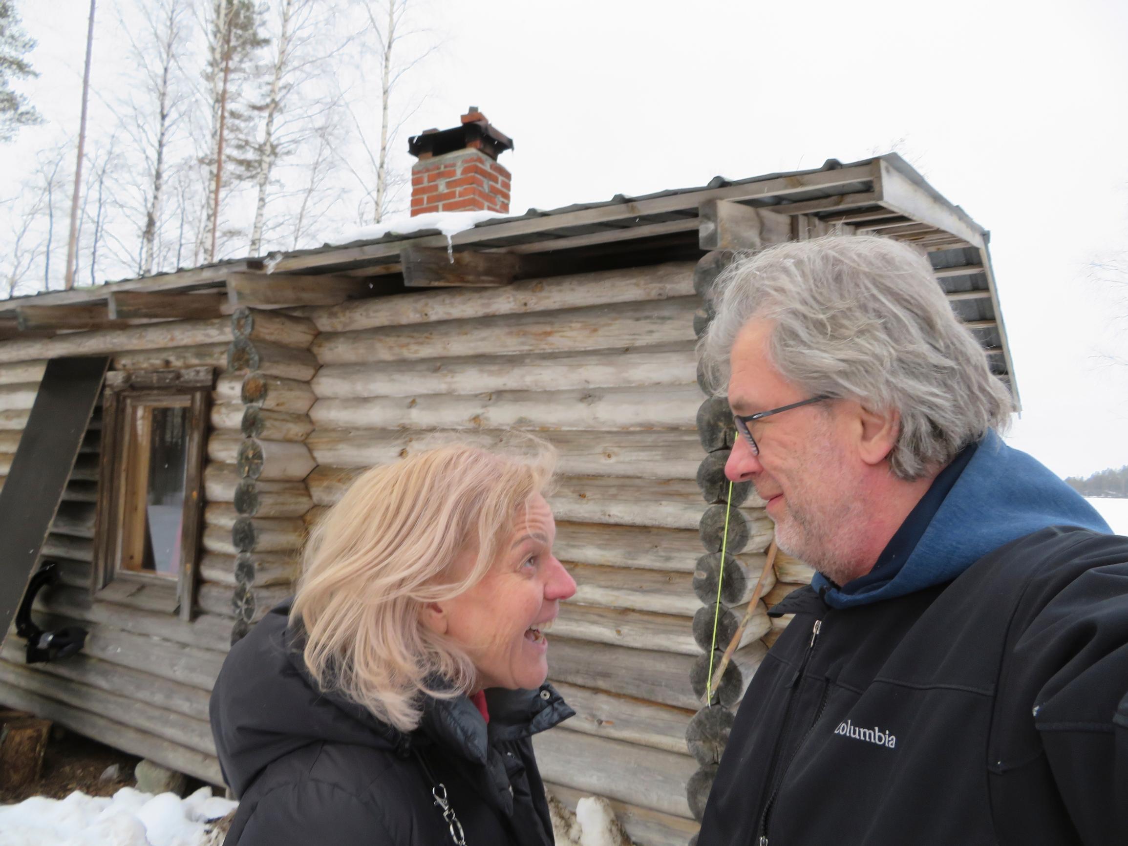 Cati Sundström katsoo nauraen Jyrki Hyytiäistä talvella hirsimökin edessä