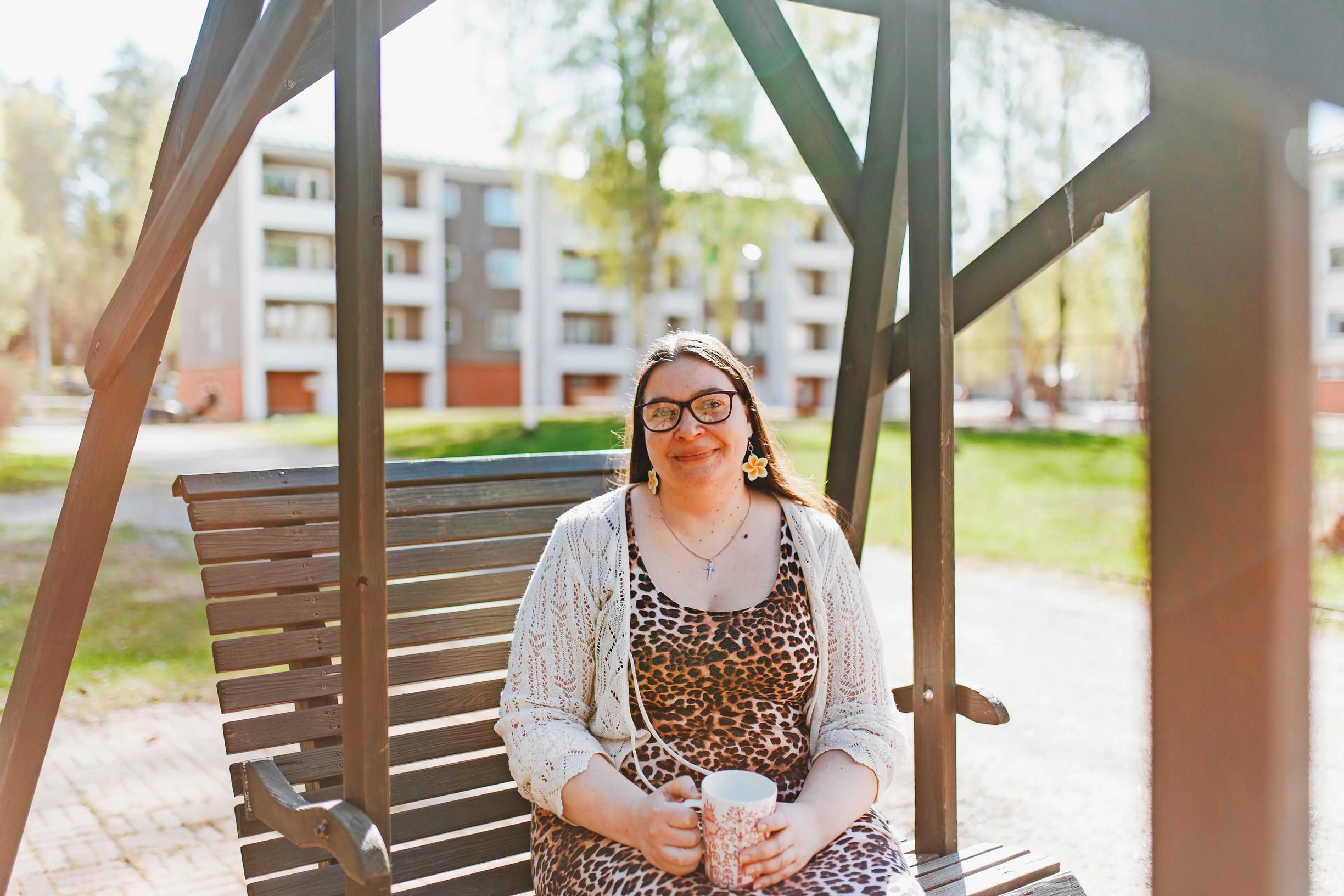 nainen istuu puutarhakeinussa muki kädessään