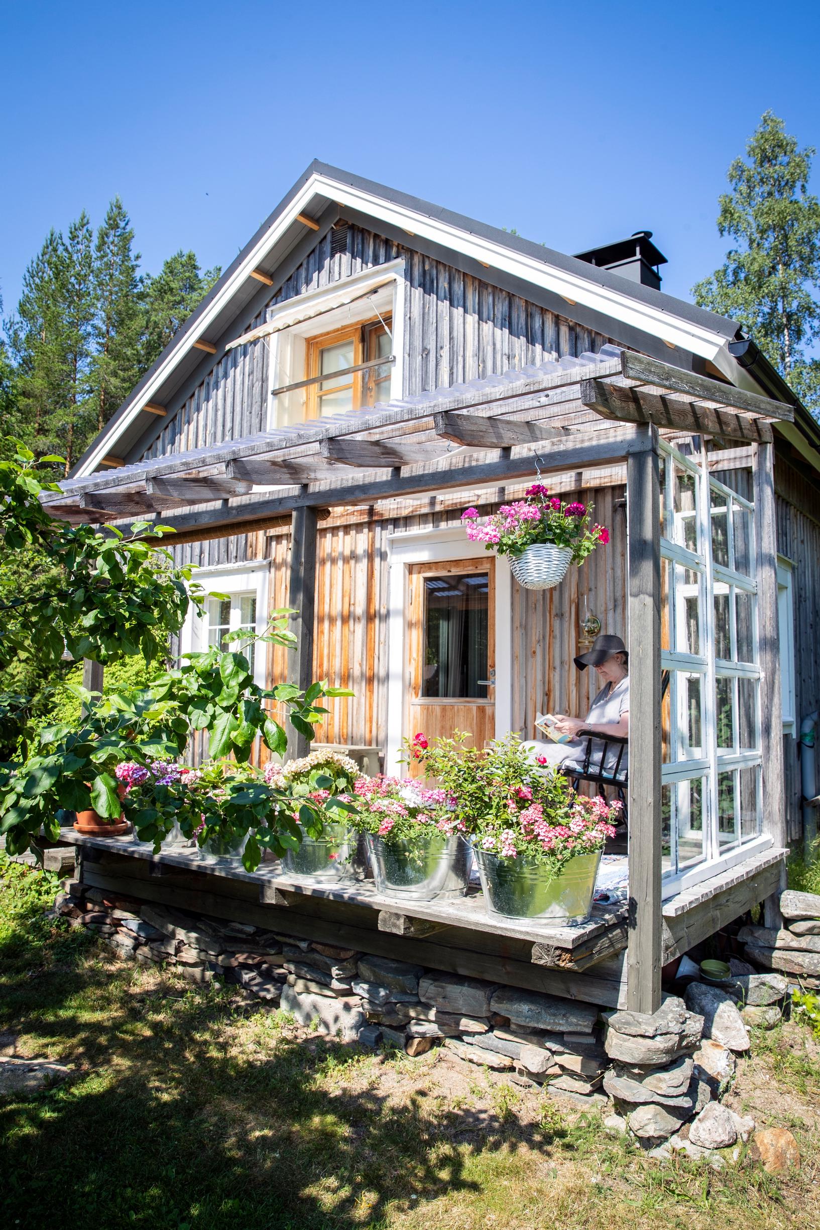 Nainen istuu harmaantuneen hirsitalon terassilla.