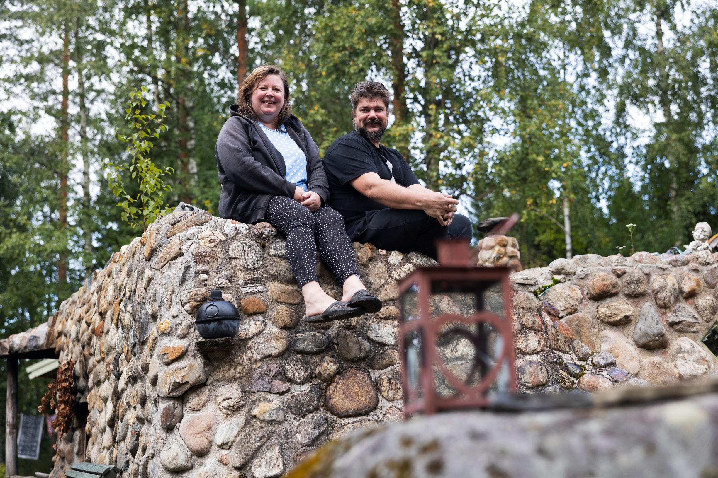 Anne ja Juha Turunen istuvat luonnonkivistä muuratun savusaunan katolla ja hymyilevät.