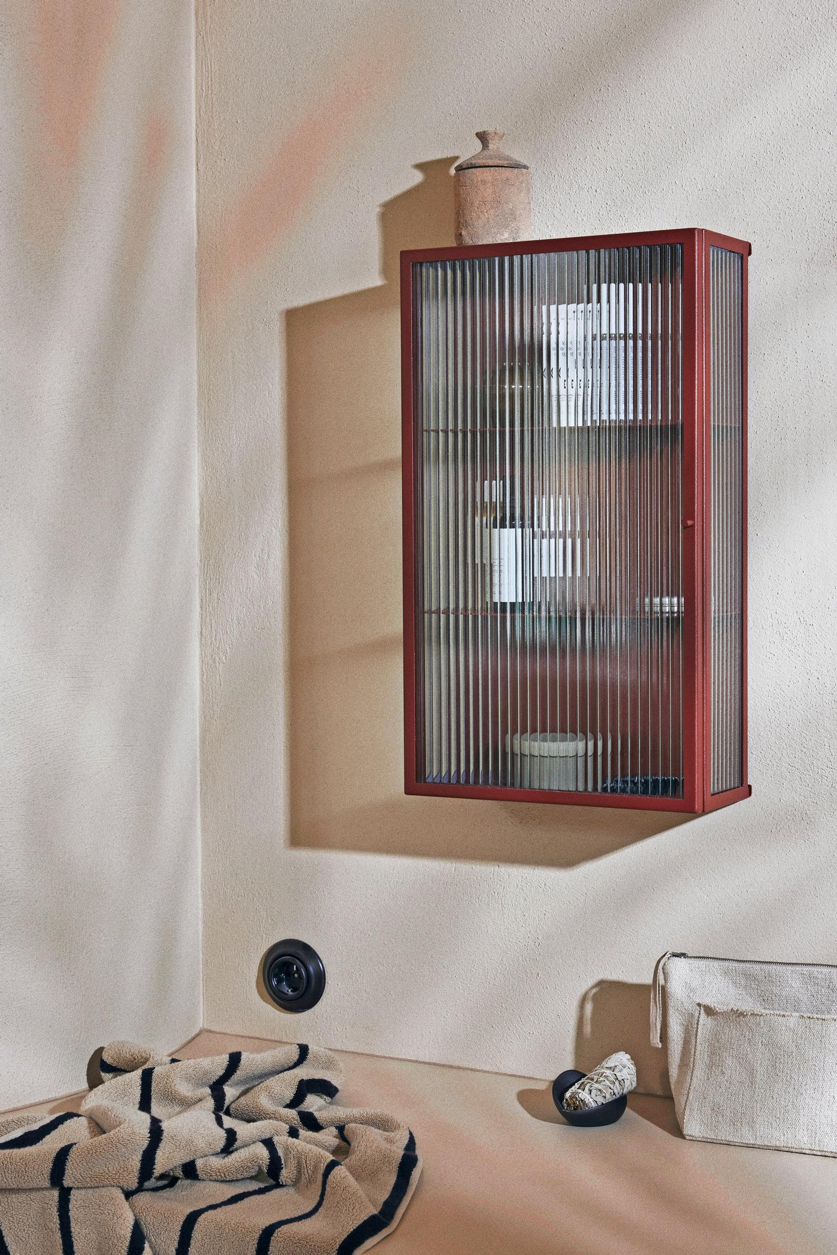 Ferm Livingin seinäkaappi Haze, jossa teksturoitu lasiovi, kaapin sisällä kosmetiikkaa, pöydällä pyyhe ja kylppärin tavaroita